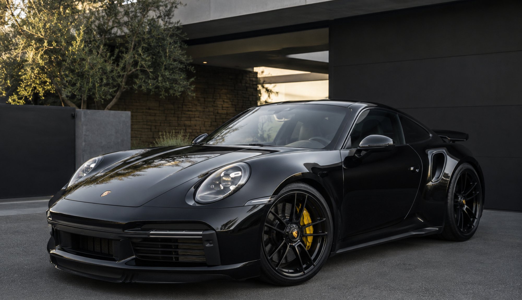 A black Porsche 911 Turbo S outside a modern house at dusk